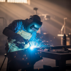 Soldador con máscara protectora y delantal, realizando trabajos de soldadura con chispas luminosas en un taller industrial de Herrería en Málaga.
